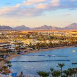 Naama Bay beach in Sharm El Sheikh with turquoise Red Sea water, golden sand, and seaside resorts