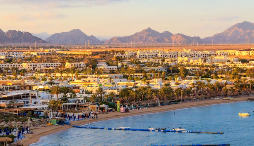 Naama Bay beach in Sharm El Sheikh with turquoise Red Sea water, golden sand, and seaside resorts